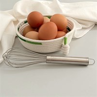 Green trimmed rope bowl filled with eggs with whisk and teatowel